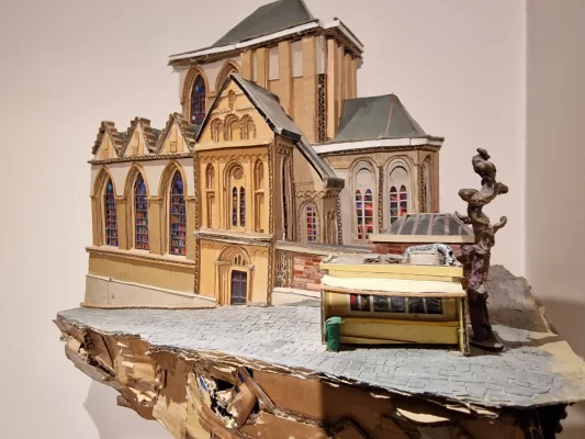 «Friture de la Chapelle» (colle, carton et divers, 2017; collection Home Frit' Home) de Yorick Efira condense en maquette le geste typiquement belge qui consiste à appuyer une baraque à frites contre un lieu sacré monumental: ici, la Friture de la Chapelle réchauffe en toute saison l'église paroissiale Notre-Dame de la Chapelle (Bruxelles). Friture-Chapelle_Yorick-Efira_WEBP